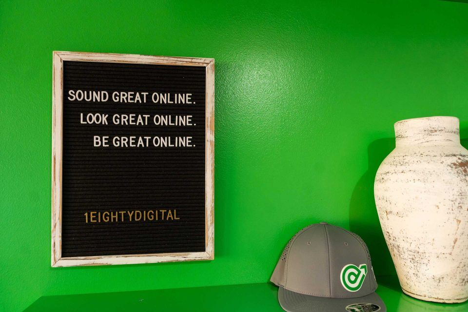 1Eighty Digital sign with motivational phrases by a hat and vase on green shelf.