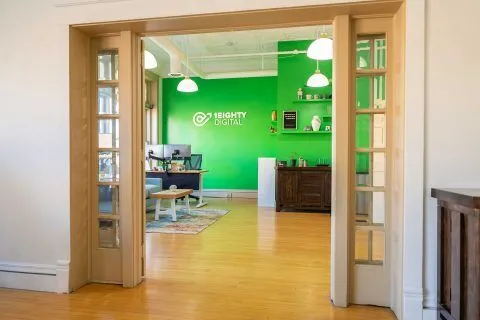 Office space with a green accent wall, branded with the 1Eighty Digital logo.