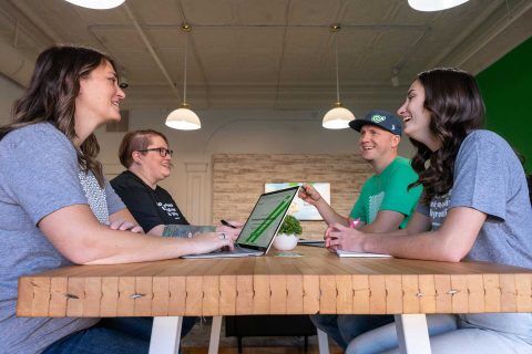 1Eighty Digital team smiling around a wooden table with a laptop.