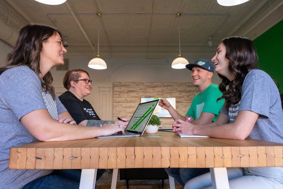 1Eighty Digital team smiling around a wooden table with a laptop.