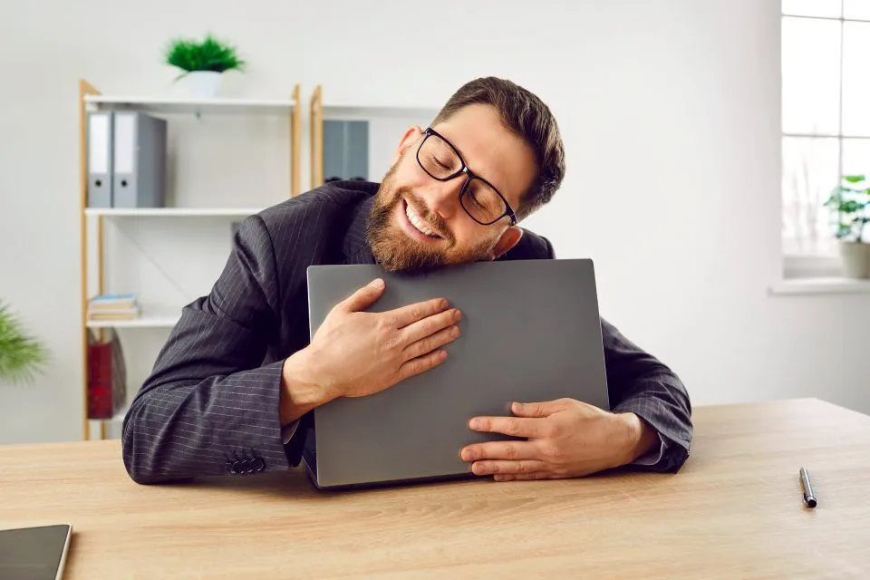 Man in suit smiling while hugging a laptop, pondering internal linking for SEO.