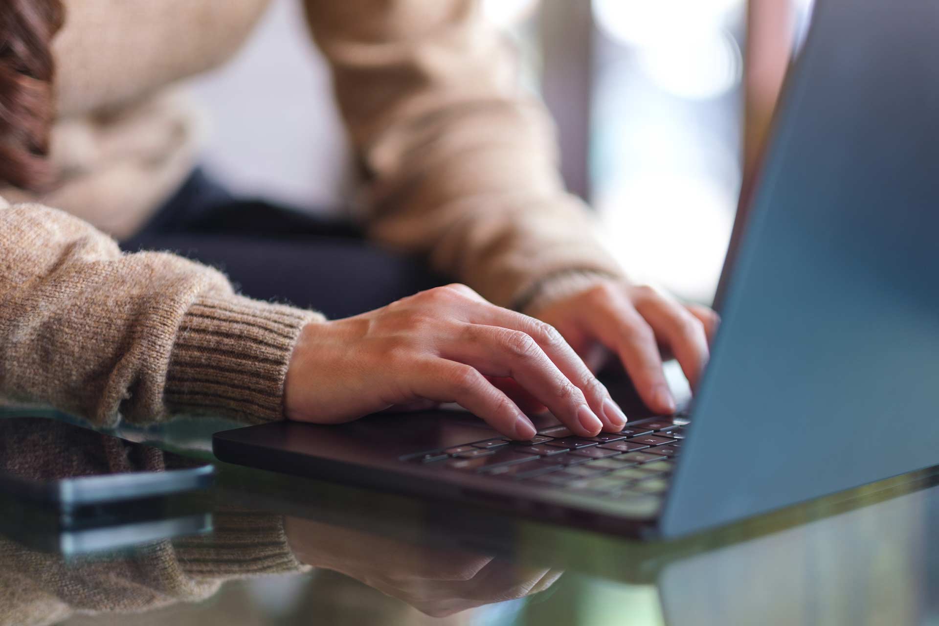 Person typing on a laptop at a glass table, doing a social media profile audit.