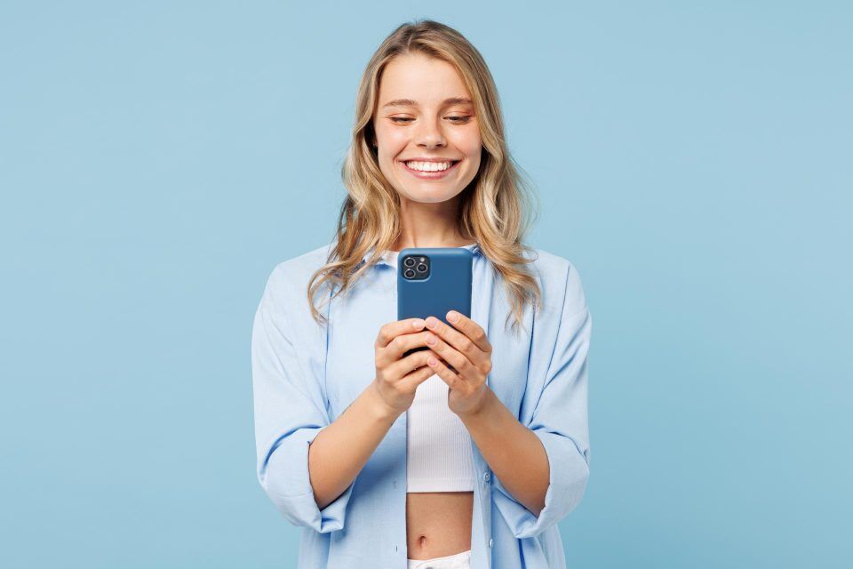 Smiling woman in blue shirt holding a smartphone, reflecting mobile-first design.
