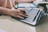 Person typing on a laptop, working on online content writing at a desk.