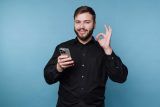 Man in black shirt holding smartphone, gesturing OK—perfect for email subject lines.