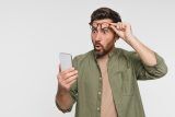 Man lifting glasses, surprised by digital marketing account setup on smartphone.