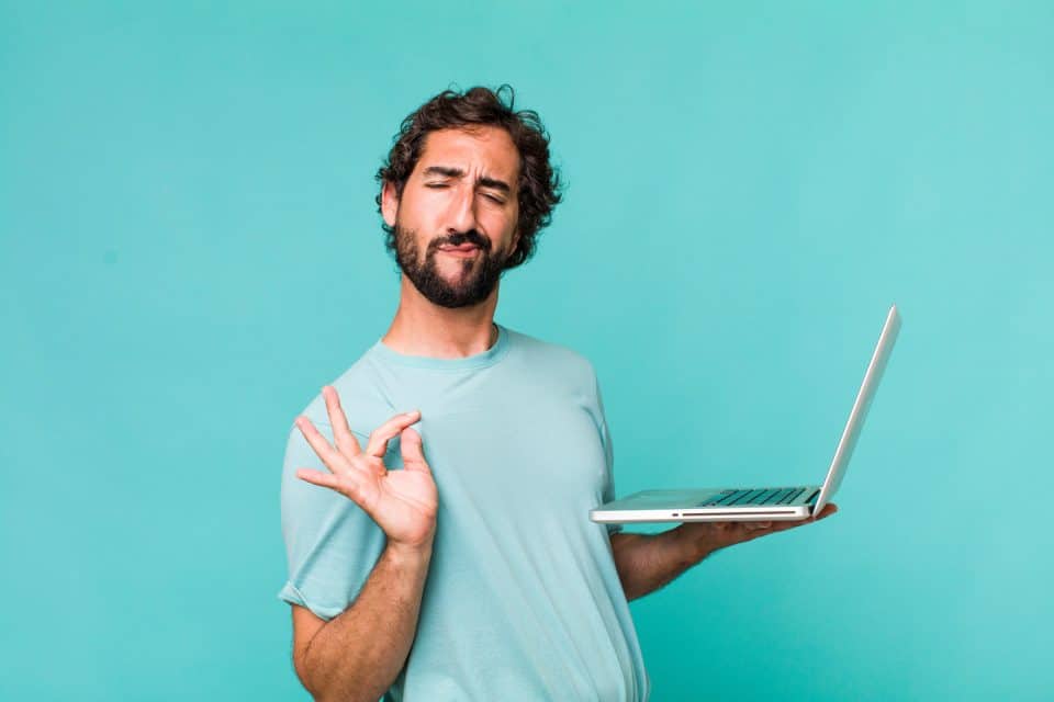 Man in a light blue shirt holding a laptop, making an OK gesture for digital marketing.