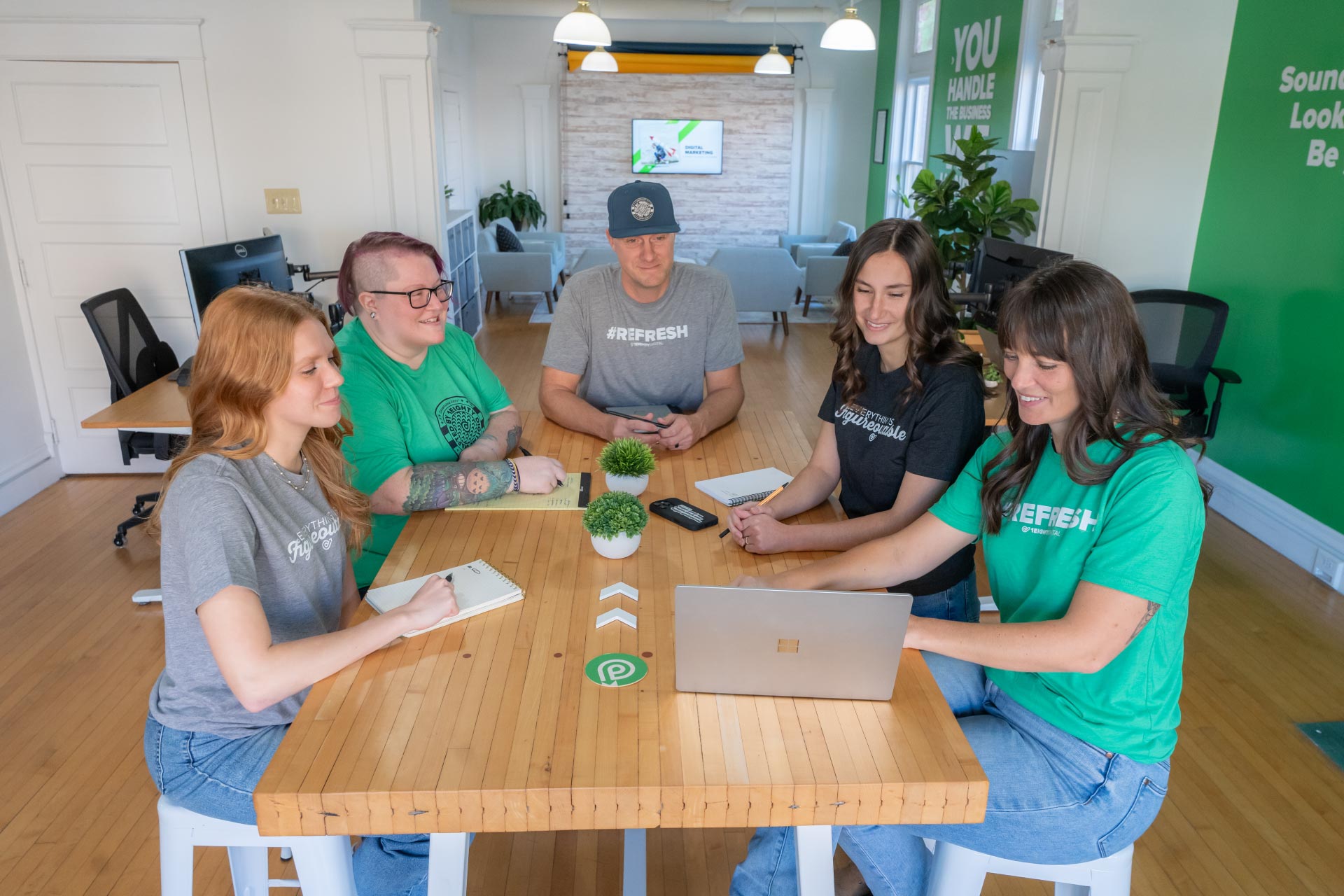 Five people discuss outsourcing digital marketing in a brightly lit office space.