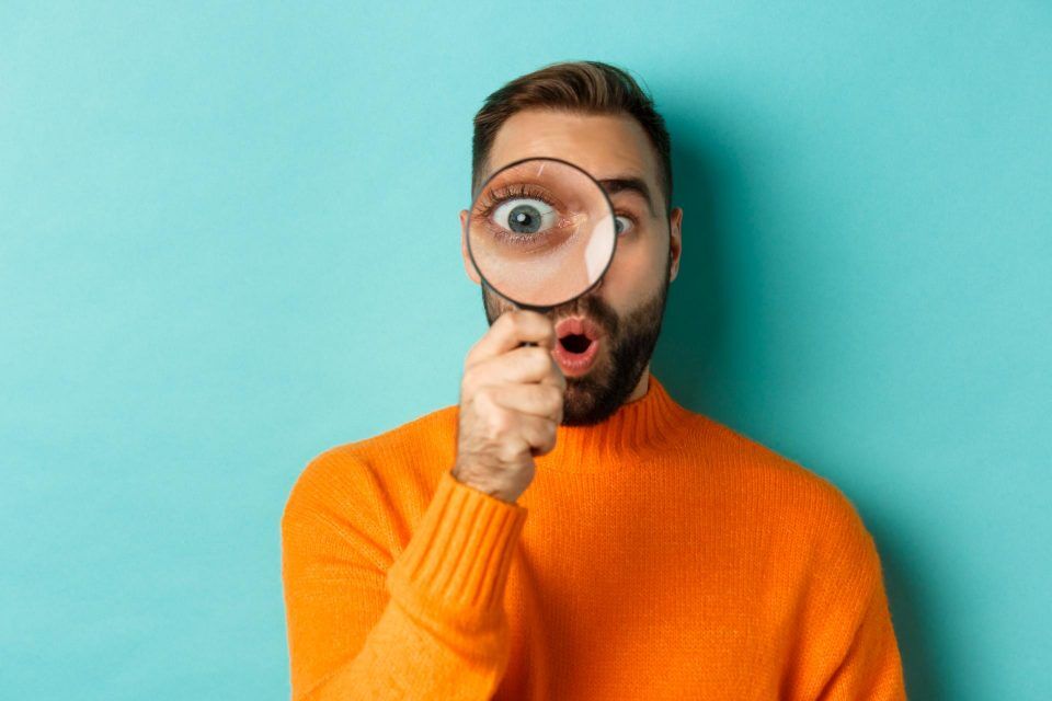 Man in orange sweater holding magnifying glass, symbolizing voice search optimization.