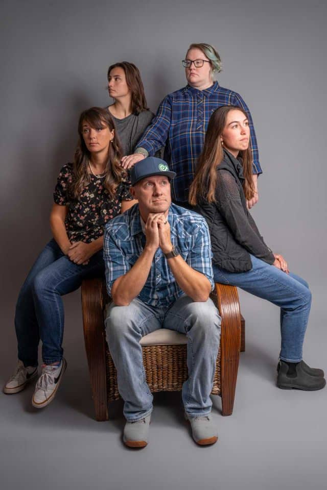 Five people pose together in a studio with neutral expressions.