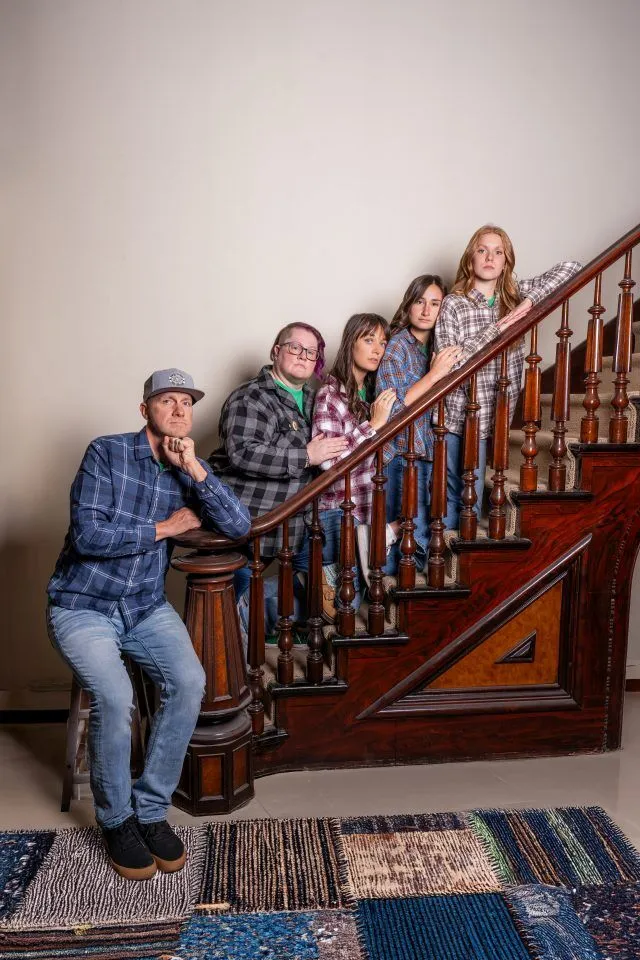 Five people in plaid shirts pose by a wooden staircase—meet the team.