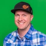 Meet the team: Smiling in a cap and plaid shirt against green.