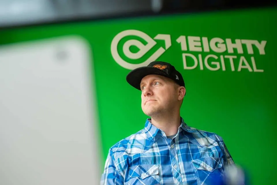 Person in blue plaid shirt, cap; green background with 1Eight Digital logo.