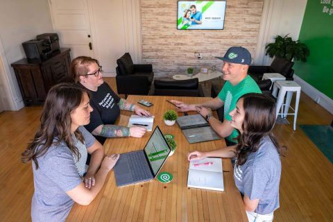 Four people having a meeting around a table with laptops and notebooks.