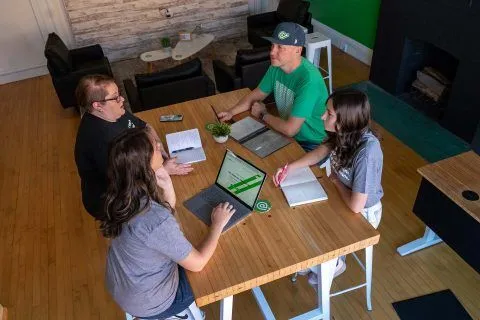Four people having a meeting around a table with laptops and notebooks.