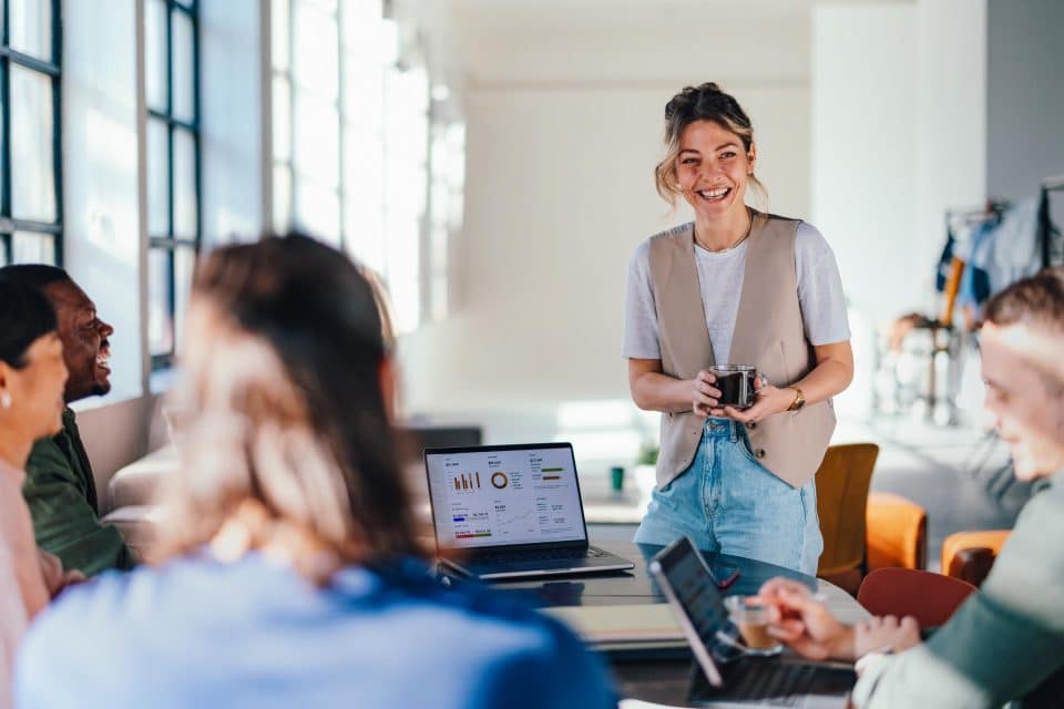 Person smiling while presenting to colleagues in a meeting room.
