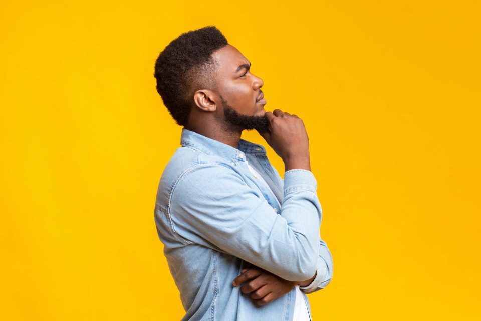 Man in profile, pondering social media marketing, against yellow backdrop.