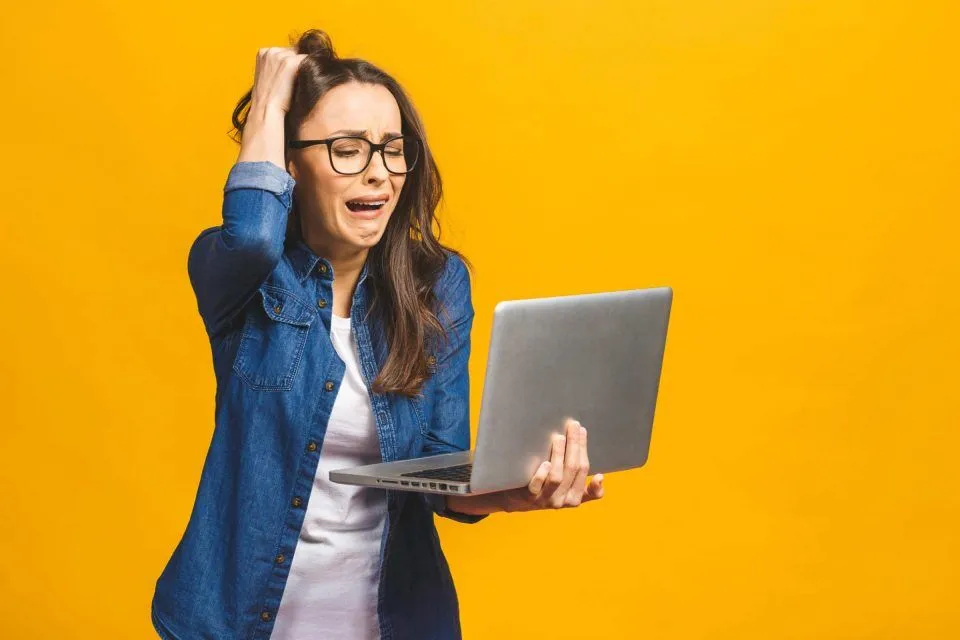 Woman frustrated by website speed while looking at laptop, yellow background.