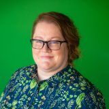 Meet the team: Person with glasses smiling in front of a green background.