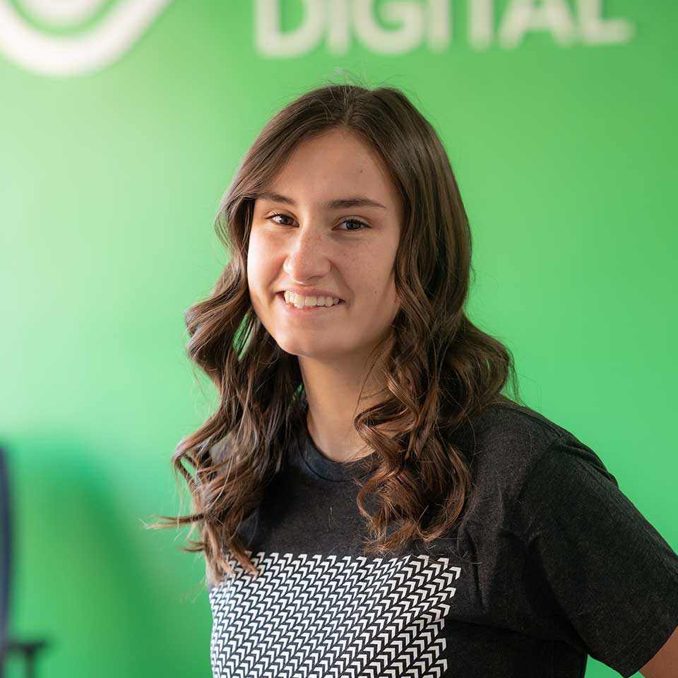 Person smiling in front of a green wall with white text behind.