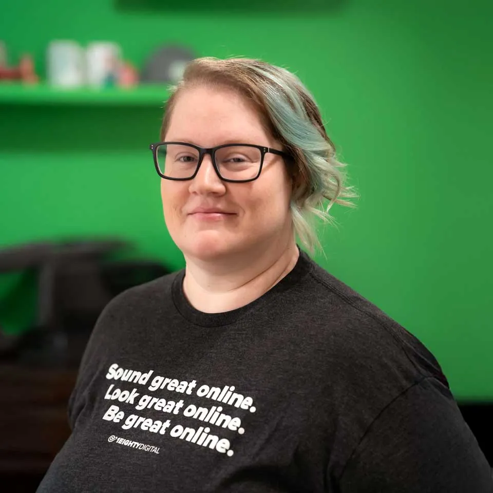 Person with glasses standing in front of a green background.