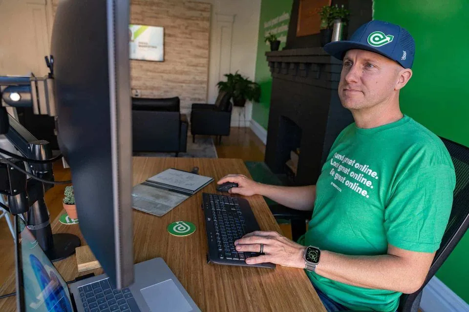 Person in green shirt and cap working at a computer in a modern office.