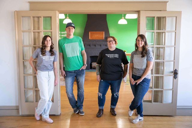 Four people standing in a room with green walls and wooden floor.
