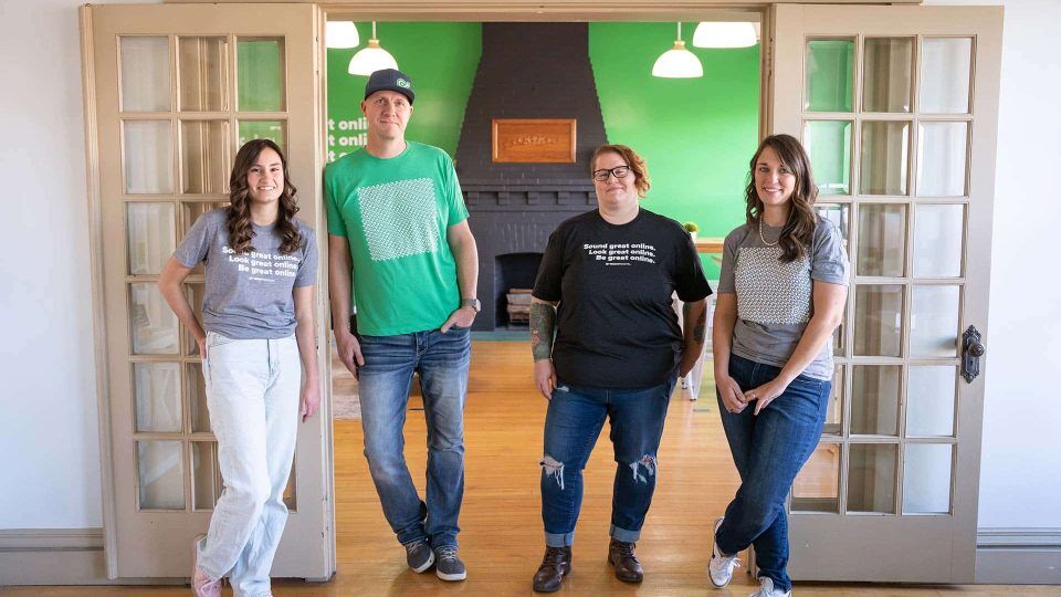 Four people standing in a room with green walls and wooden floor.