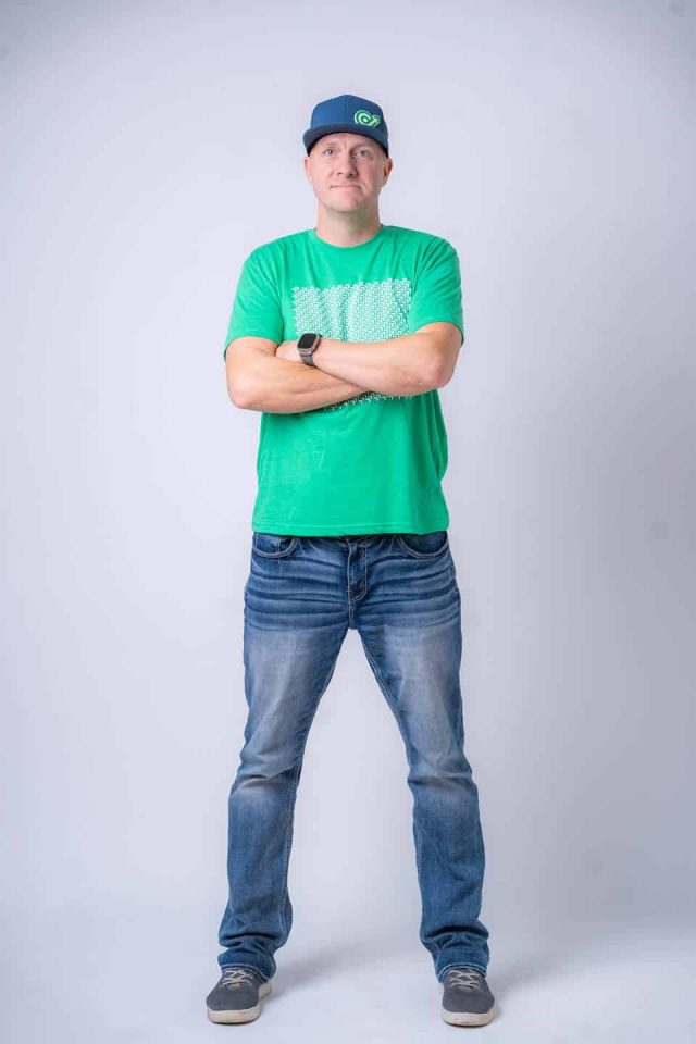 Person standing with arms crossed, wearing a green shirt and blue cap.