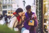 Three women smiling, holding gifts on a festive street; perfect holiday marketing.