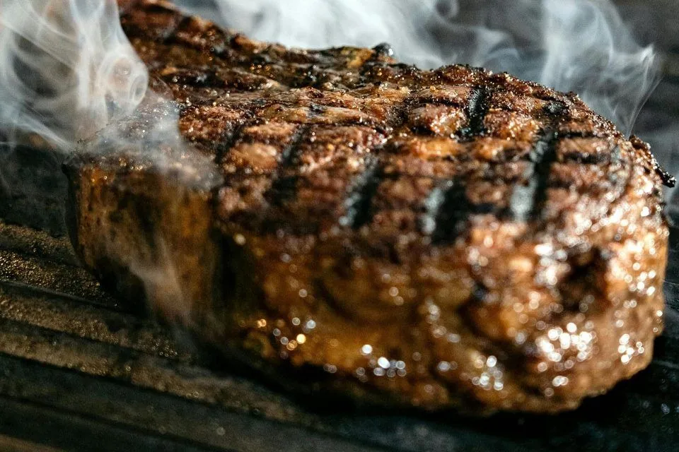 A grilled steak with char marks and visible smoke rising from it on a grill.
