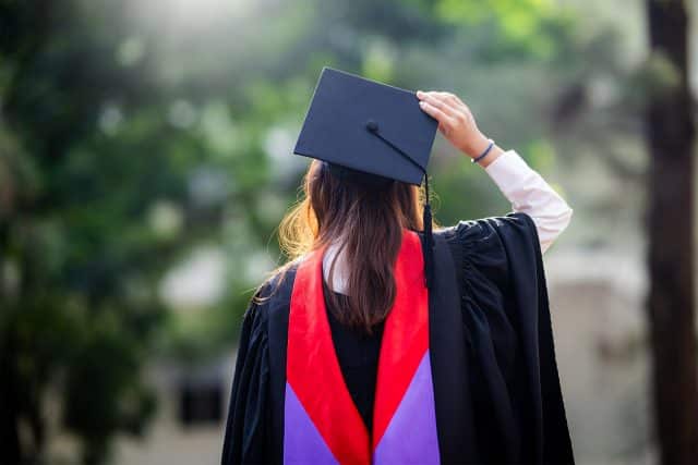 Graduate in cap and gown, adjusting cap, with Kosciusko Foundation backdrop.