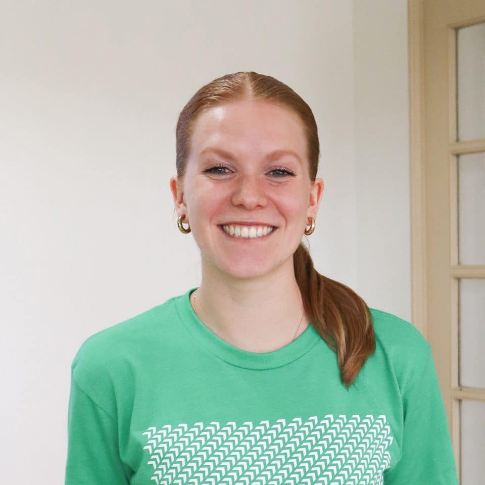Person in green shirt smiling in a neutral indoor setting.