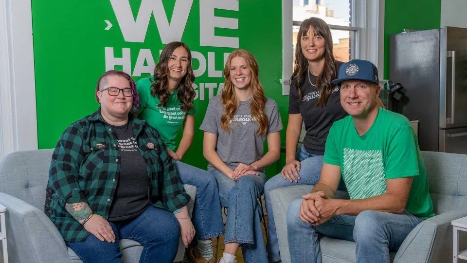 Five people sit together in a modern office with green and white wall signage.