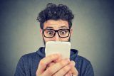 Person with glasses, surprised by smartphone screens marketing services.