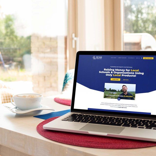 Laptop on table with a blue barn fundraising website and coffee cup nearby.