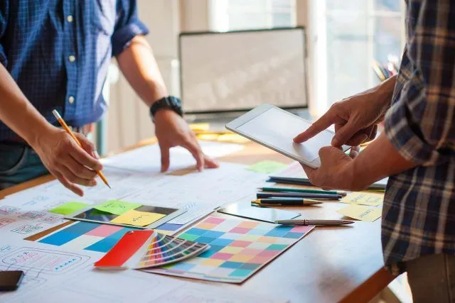 Two people discussing Blue Note Design plans and a color palette on a table.