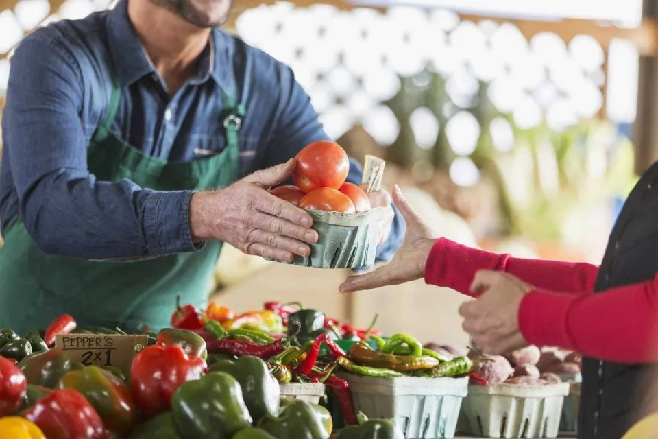 Columbia City vendor hands tomatoes to customer at a market stall.