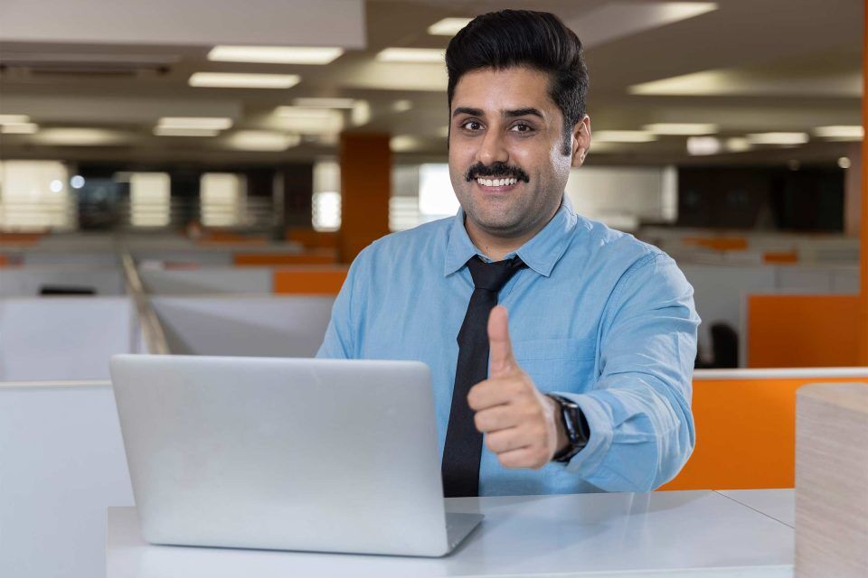 Person in blue shirt gives a thumbs up near laptop; is your website credible?.