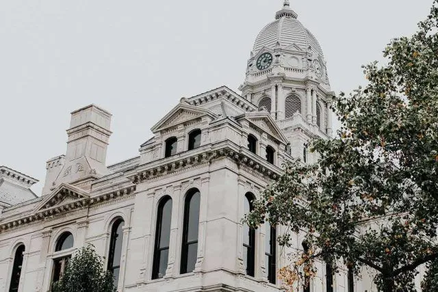 Historic white stone building with a clock tower and trees in the foreground.