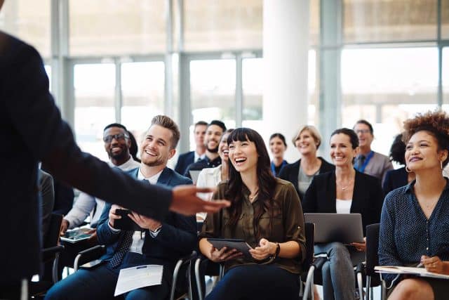 Audience smiling and clapping during EVI Training in a bright room.