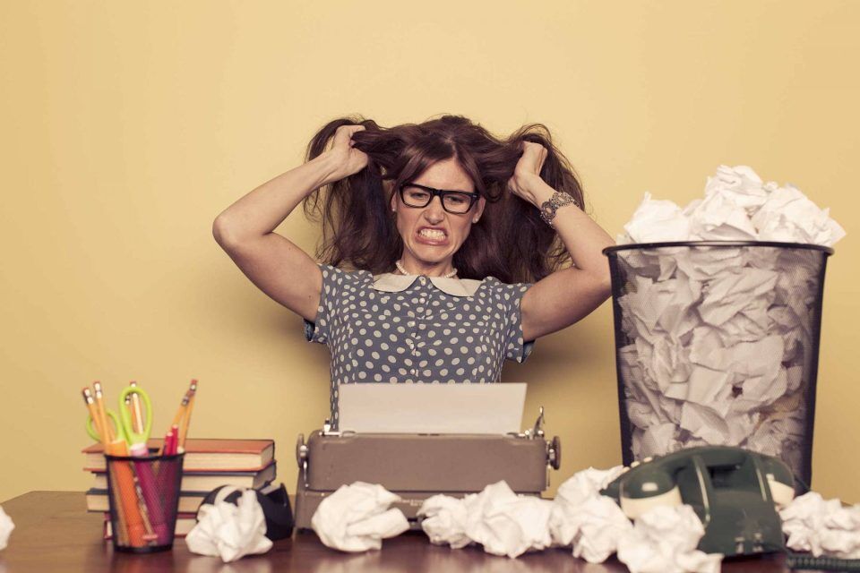 Website content writer frustrated, surrounded by crumpled papers and books.