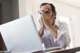 Man with glasses rubs eyes in front of laptop, Facebook mistakes evident.