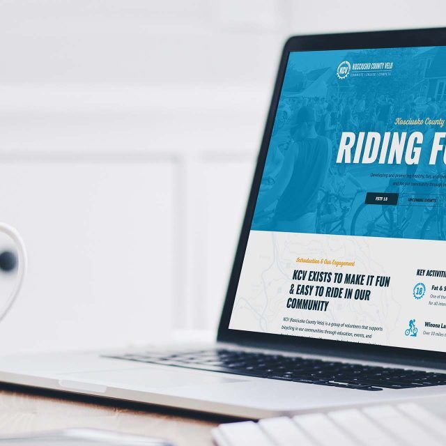 Laptop displaying a Kosciusko County Velo site next to a coffee mug.