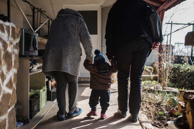 Two adults and a child, hand in hand, on a porch walkway with lost sparrows.