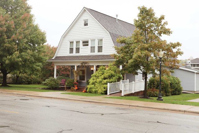Two-story white house by Pottery Bayou, featuring a porch and ramp, tree-lined.