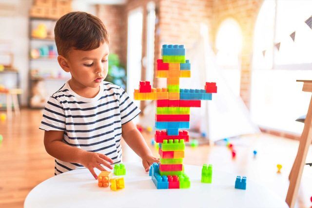 Child at Presby Preschool builds a colorful block structure on a white table.