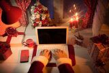 Santa in suit typing holiday email marketing, surrounded by gifts and candles.