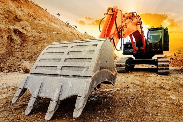 Large excavator at sunset, powering SiteWorx Services construction site.