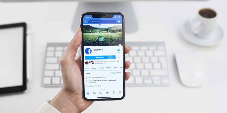 Hand holding smartphone displaying social media platform, keyboard in background.